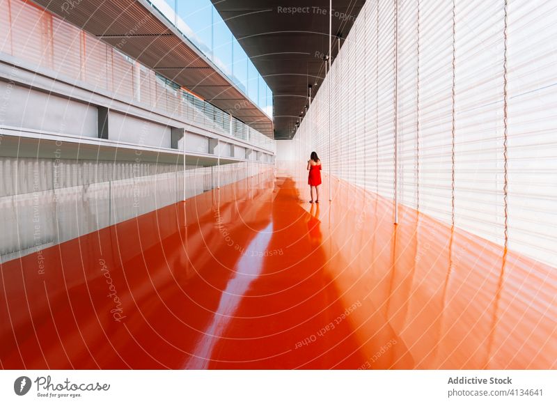 Anonymous woman in spacious corridor in minimal style hallway interior orange color vivid design geometry female passage futuristic contemporary modern vibrant