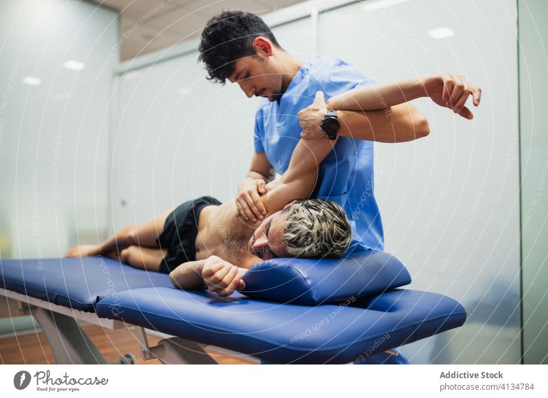 Orthopedist with mask stretching arm of sportsman during medical checkup orthopedist patient recovery examine professional osteopathy aid health care