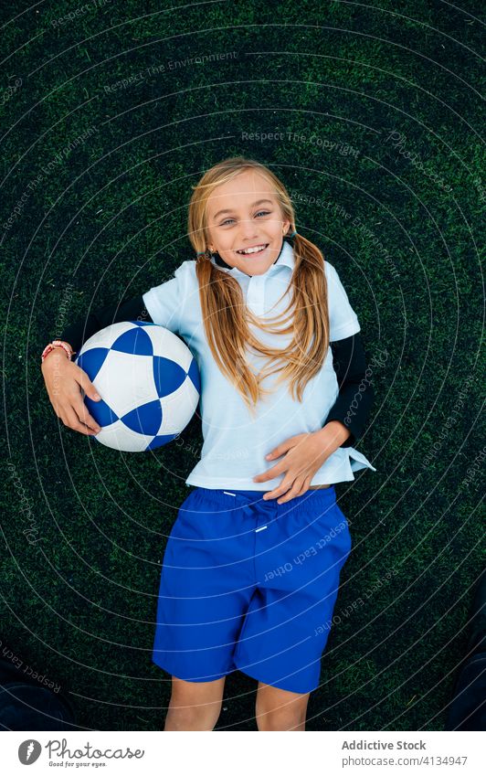 Cheerful girl player with soccer ball relaxing on lawn laugh field football ponytail stadium child kid preteen happy playful optimist uniform equipment sporty