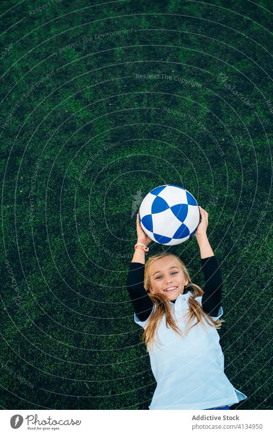 Pleased young female player tossing ball up while lying on football field girl soccer having fun rest child kid stadium relax exercise equipment training catch