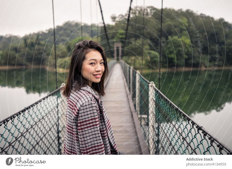 Calm Asian female traveler standing on suspension bridge over river tourist forest adventure tourism vacation picturesque peaceful journey serene reflection