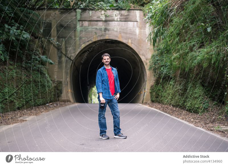 Male traveler in jeans taking photo near green mountain tourist photo camera take photo road tunnel vacation tourism photographer using digital device holiday