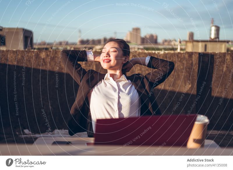 Cheerful woman having break during remote work with laptop relax busy rest rooftop workplace young asian female employee ethnic formal device gadget freelance