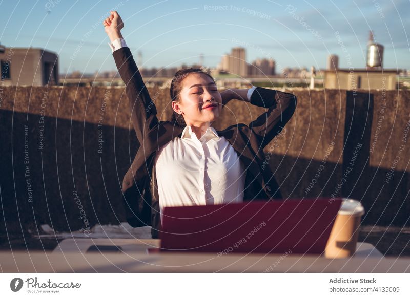 Cheerful woman having break during remote work with laptop relax busy rest rooftop workplace young asian female employee ethnic formal device gadget freelance