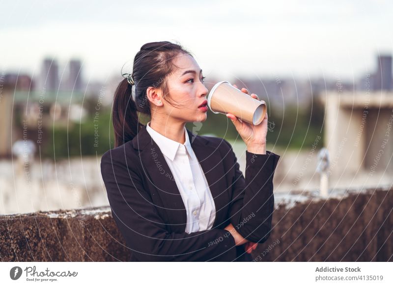 Young business woman drinking a takeaway coffee businesswoman serious focus break young asian ethnic formal disposable cup rooftop to go modern female