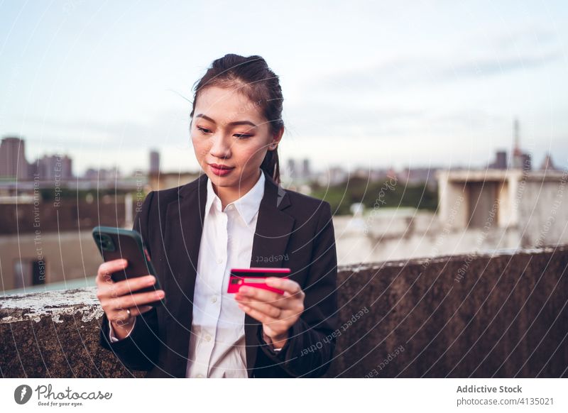 Busy ethnic woman with credit card and smartphone busy serious problem using formal young asian businesswoman customer rooftop city device female gadget