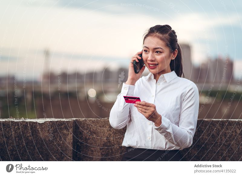 Busy ethnic woman with credit card speaking on phone phone call busy serious talk smartphone problem discuss formal young asian businesswoman conversation