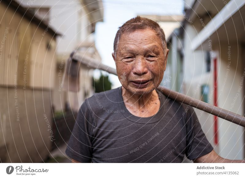 Senior ethnic farmer with hoe on street in township senior man gardener appearance smile portrait oriental tool urban taiwan personality local aged district