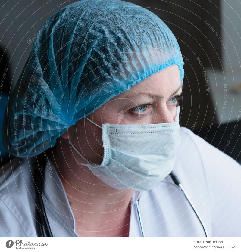 Medical woman face close up. Doctor in a medical mask and gown. She looks tired. She looks out the window. Horizontal composition doctor paramedic women