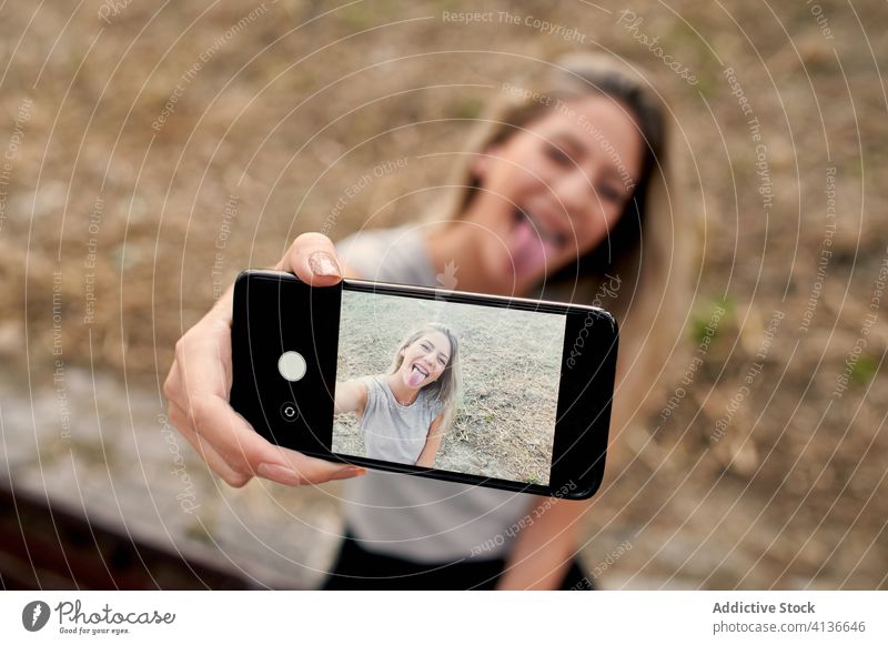 Cheerful woman taking selfie on smartphone cheerful make face show tongue having fun young street playful happy photo device gadget screen lifestyle mobile