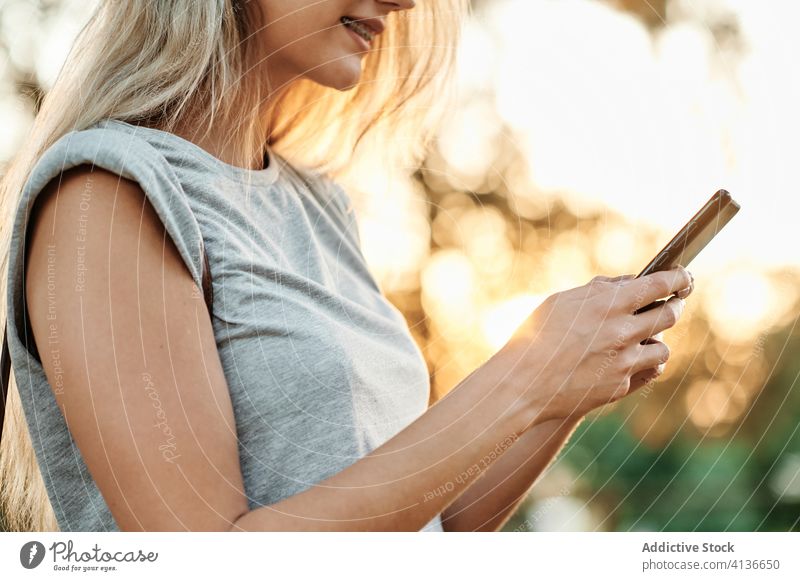 Anonymous woman with smartphone standing in park using enjoy browsing young female trendy lifestyle gadget device chill positive social media smile online
