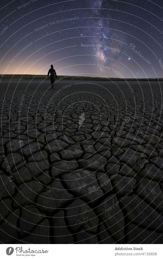 Anonymous male standing on dry desert in starry night man sky milky way drought silhouette nature surface crack landscape scenery tourism travel global warm