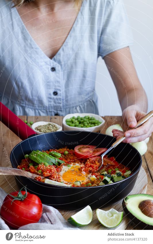 Crop woman eating tasty shakshuka in kitchen egg vegetable enjoy breakfast ingredient dish pan calorie female tradition quinoa tomato sit delicious cuisine