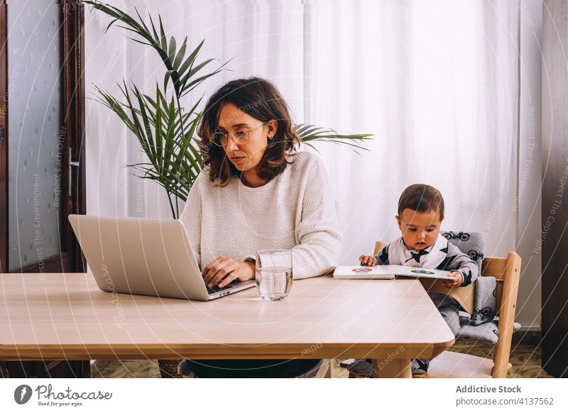 Mother working with laptop at table with kid woman home using busy mother online remote modern young female together baby internet browsing device gadget child