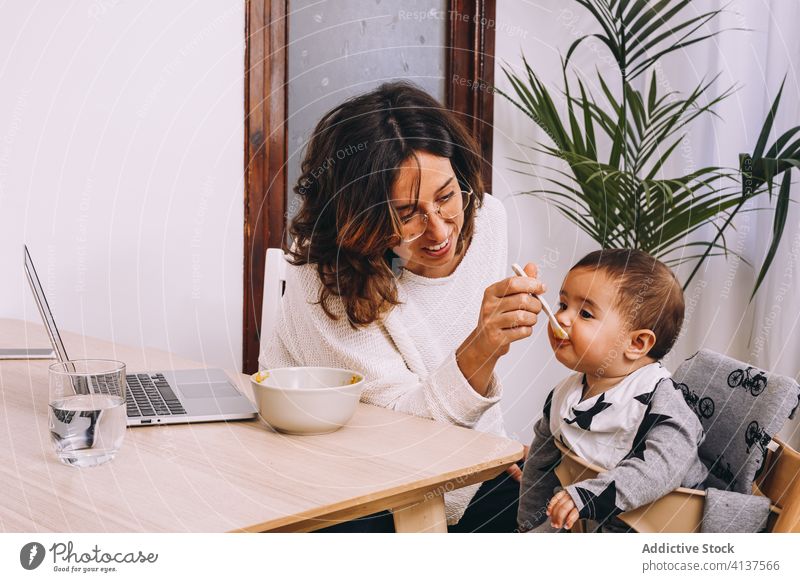 Busy mother feeding kid and working from home woman laptop busy modern connection interact young female baby device gadget child multitask lifestyle freelance