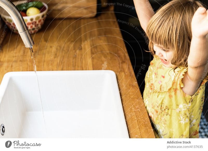 Delighted girl having fun near sink child wash smile arms raised wet water kitchen home tap counter kid cozy lifestyle domestic routine childhood fresh harmony