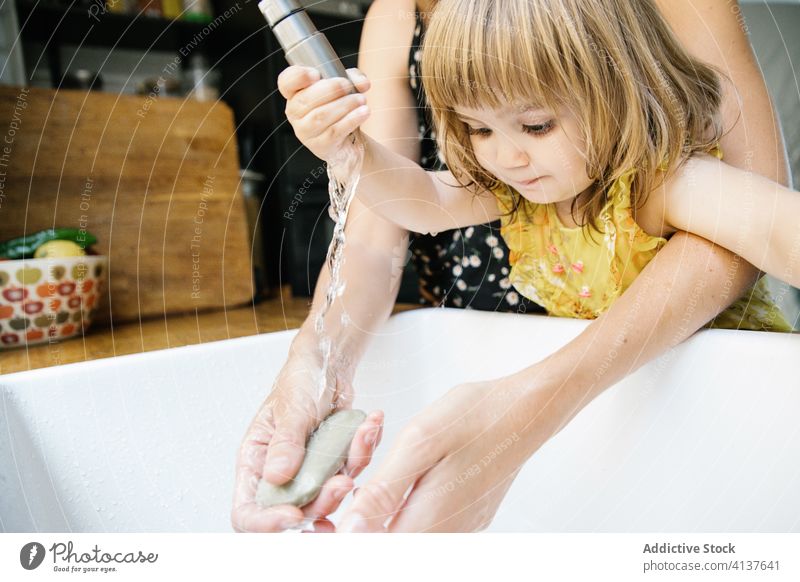 Mother and daughter interacting with water tap mother sink wash hand teach kitchen home hug embrace little lifestyle childhood domestic kid together parent help