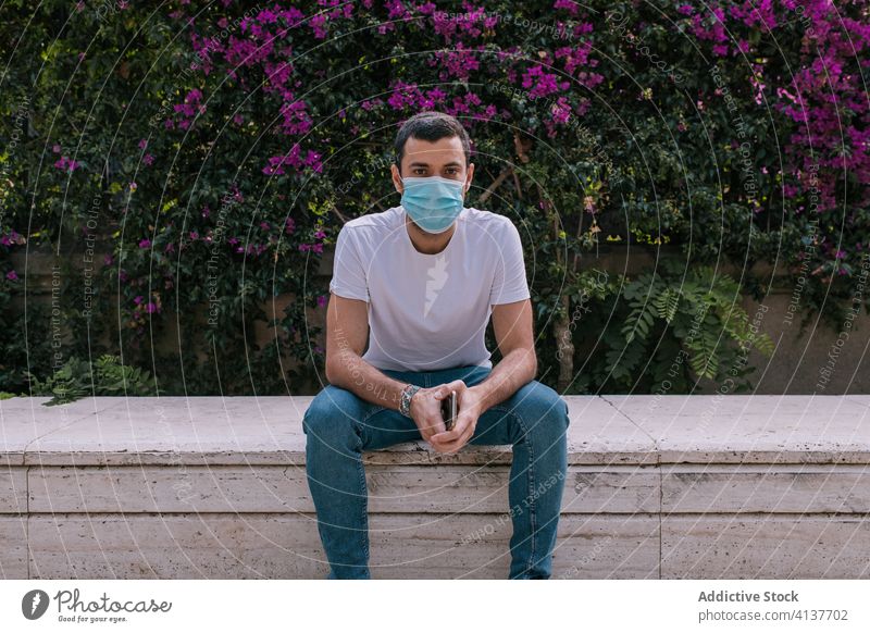 Young man wearing a face mask outdoors during a pandemic street corona virus protection young city person crisis worried distance sitting europa health public