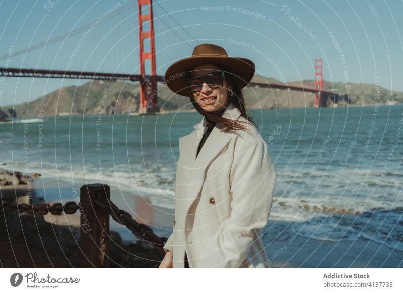 Stylish woman standing on waterfront with bridge in background trendy style travel happy smile young enjoy female tourism san francisco golden gate california