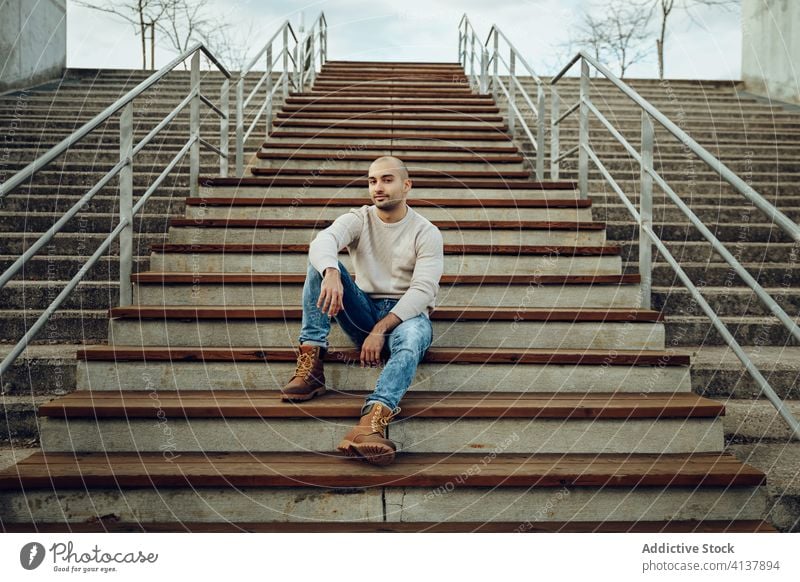 Content stylish man sitting on stairs in city style trendy hipster modern street style portrait young positive content stairway unshaven guy jeans boot casual