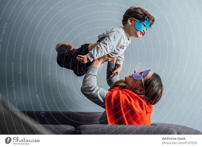 Smiling mother playing with son at home superhero toss mask game having fun boy together pretend creative playful cheerful little weekend kid child happy