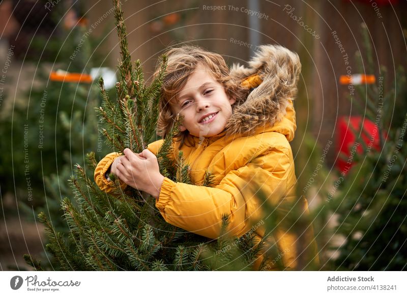 Beautiful blond boy with yellow jacket buying his Christmas tree smiling find outside pine snowy boys childhood walking seasonal young youth weather winter