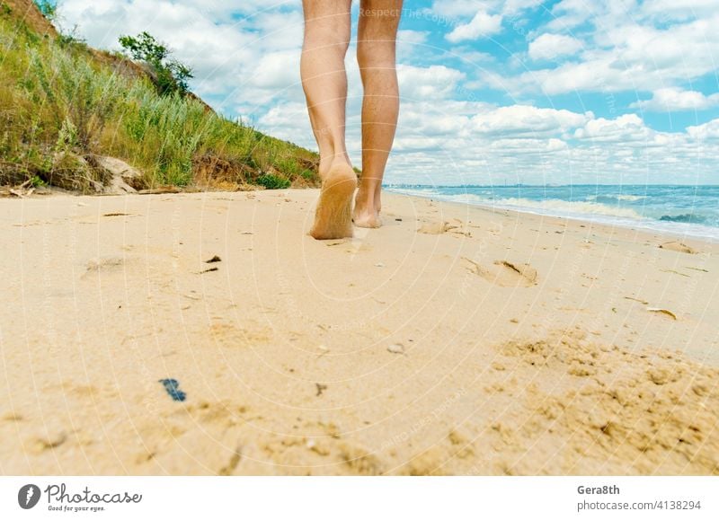 man walks barefoot along the beach towards the city adult alone bank bathing beach blue sky caucasian cloudy day day light european feet footprints journey legs