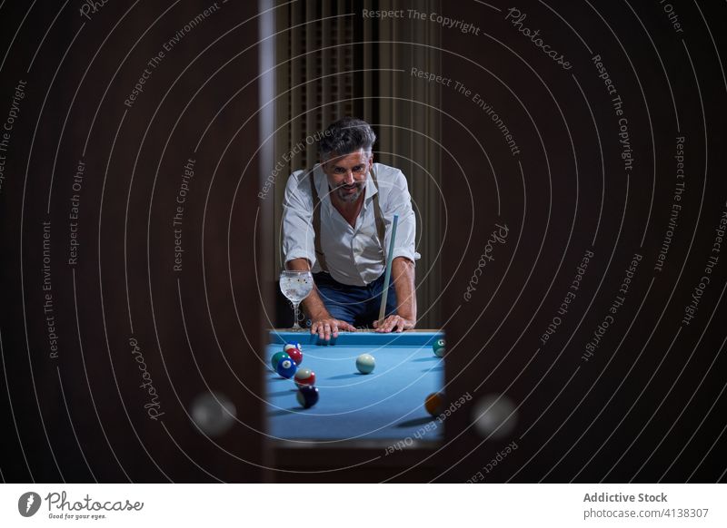 Mature man playing billiards at home pool table cue thoughtful mature game think male casual style pensive lean concentrate serious focus stand ponder cocktail