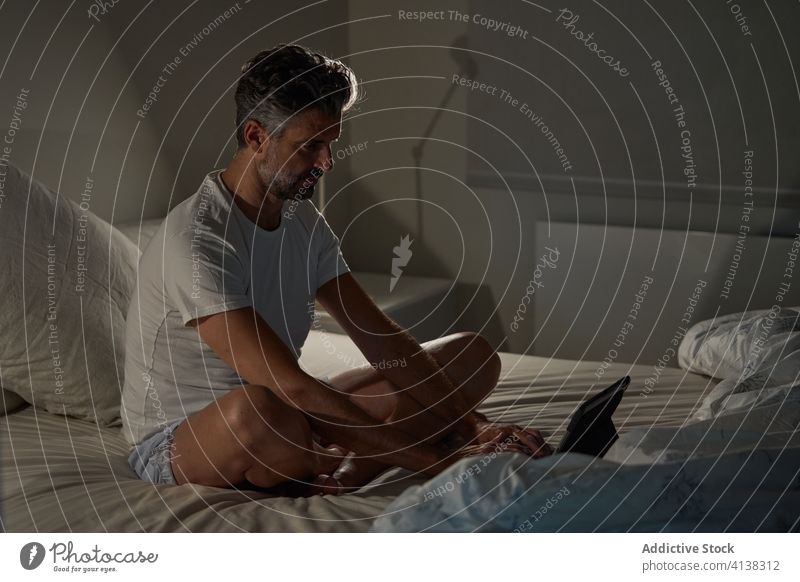 Man using laptop in bedroom man home browsing positive mature sitting rest male casual device gadget relax online internet lifestyle comfort happy connection
