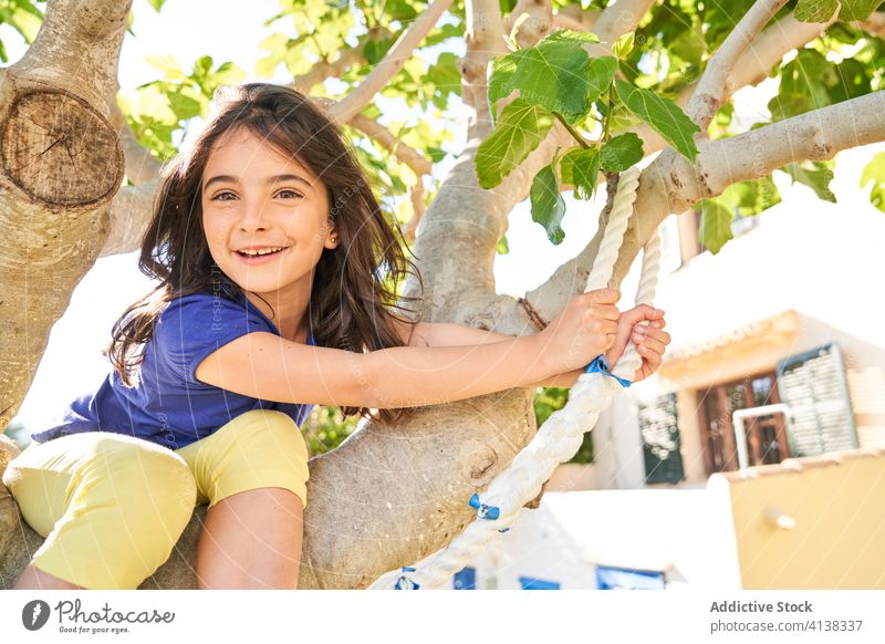 Little girl siting on tree and preparing for jump with rope kid having fun summer activity happy vacation holiday positive garden yard child prepare cheerful