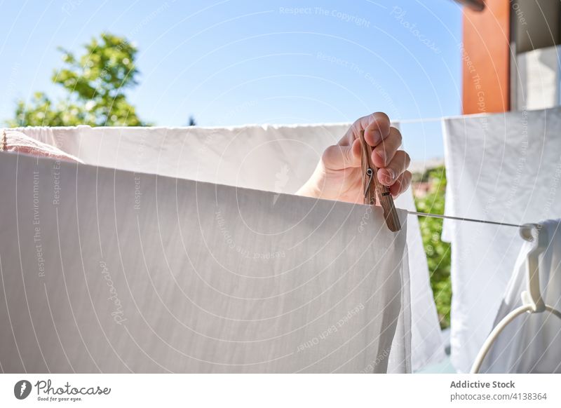 Unrecognizable person hanging clothes on rope with pegs on balcony laundry clothespin linen wet sunlight summer domestic chore housework everyday routine fresh