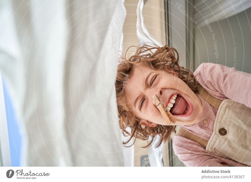 Cheerful little boy with clothespin attached to nose scream fun laundry peg pretend joke humor kid child home childhood cheerful joy game leisure amazed playful