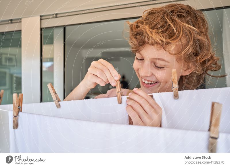 Boy at balcony and hanging laundry kid linen domestic rope chore cloth housework child home responsible smart smile overall boy apartment joy happy room window