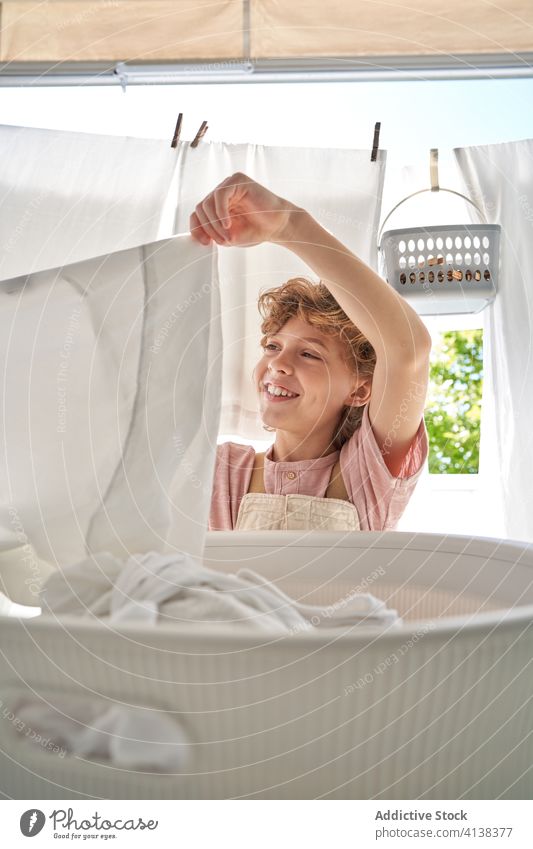Little boy with basket of linen on balcony at home wash hang laundry domestic chore kid childhood help sit everyday assist clean hygiene care cute happy work