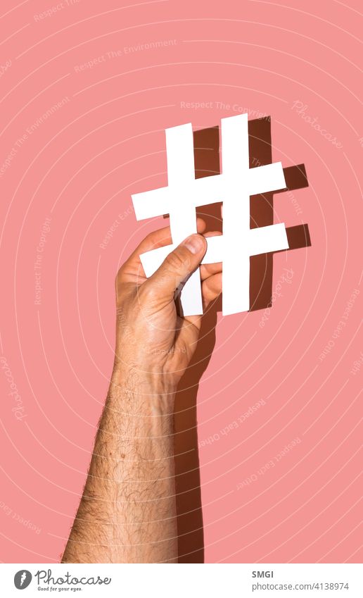 A man's hand holding a white hash on a pink background. website media social marketing male followers isolated network tag social media hashtag closeup online