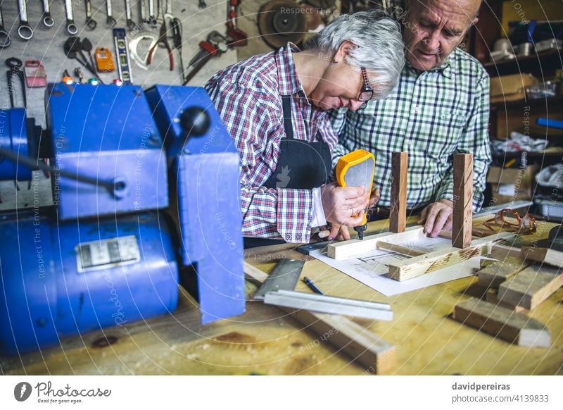Senior couple in a carpentry woman senior gluing chair diy carpenter using glue furniture workshop working wood mature business caucasian retirement worker