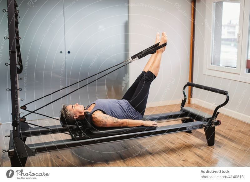 Flexible woman doing exercises on pilates reformer machine sportswoman training stretch flexible gym resist band female sportswear lying modern healthy physical