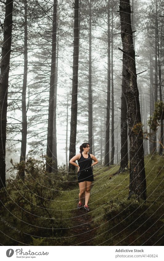 Fit woman waling along path in misty forest run walking sportswoman runner fit athlete wood training morning workout female sportswear wet pathway healthy