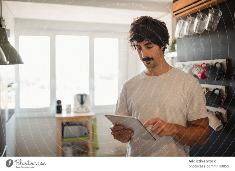 Man using tablet in kitchen browsing man modern home serious device casual internet male surfing connection online communicate social media watch gadget