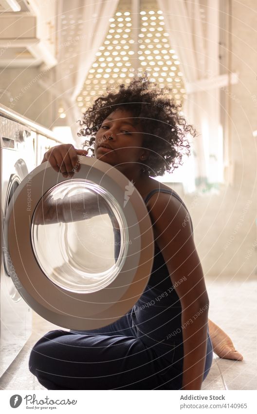 Crop ethnic woman loading washing machine at home laundry housewife kitchen domestic chore female calm clean household african america dirty casual housework