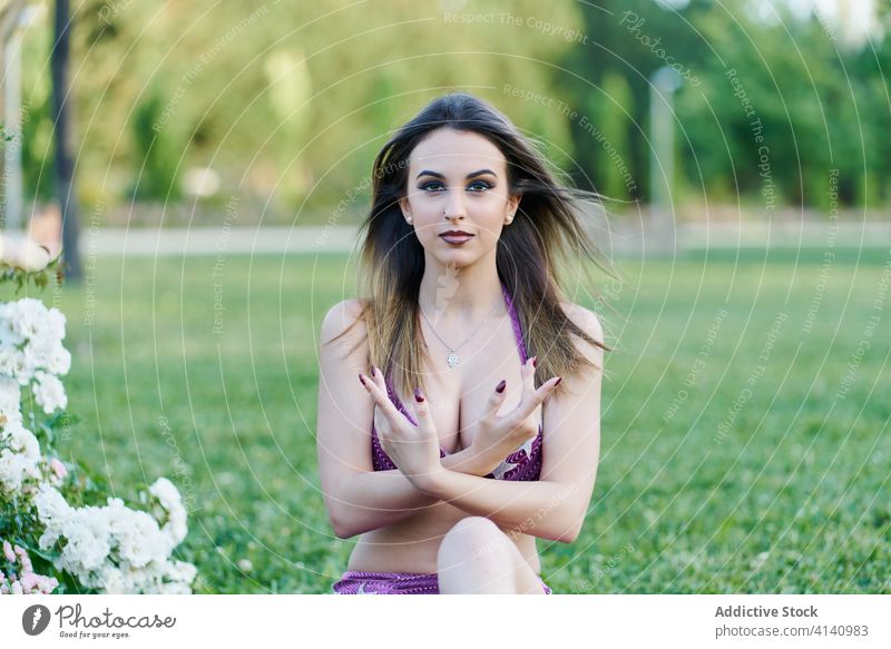 Tranquil woman in costume for belly dancing in park serene harmony relax cheerful pose female ethnic dancer calm smile lawn green practice sit grass happy