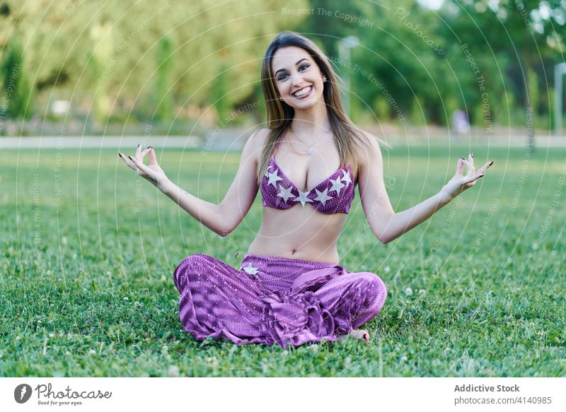 Tranquil woman in costume for belly dancing meditating in park yoga lotus pose meditate serene harmony relax cheerful padmasana female ethnic dancer calm smile