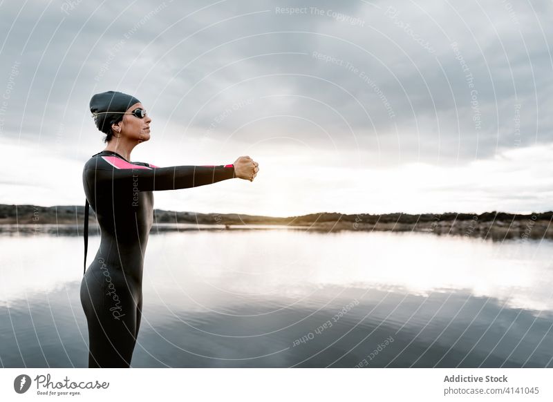 Calm woman stretching on rock on lake shore nature warm up diver wetsuit harmony calm overcast water sports wellness flexible barefoot slim healthy energy