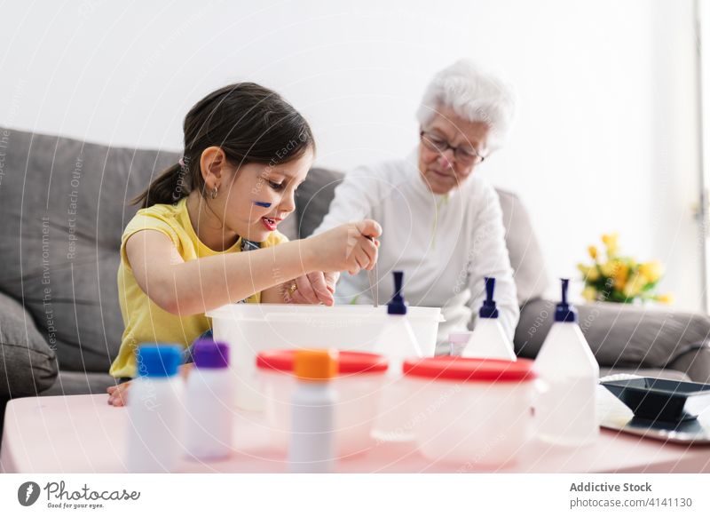 Cheerful grandmother and girl creating slime in container at home granddaughter handcraft fun diy art childcare upbringing preschool domestic together process