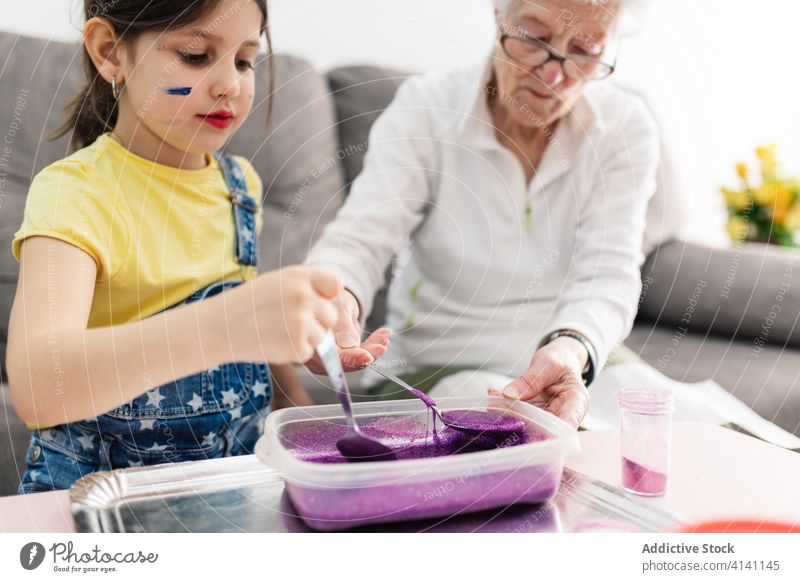 Cheerful grandmother and girl creating slime in container at home granddaughter handcraft fun diy art childcare upbringing preschool domestic together process