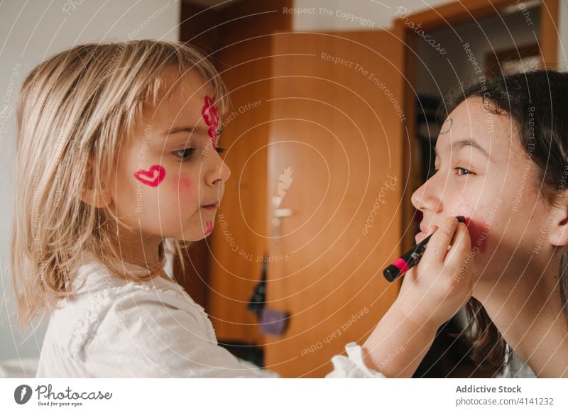 Adorable sisters with painted faces at home pastime girl sibling having fun together playful relationship kid teen little childhood cute teenage bonding cozy