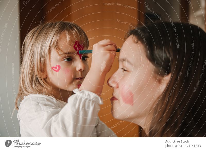 Adorable sisters with painted faces at home pastime girl sibling having fun together playful relationship kid teen little childhood cute teenage bonding cozy