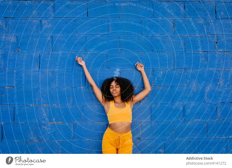 Dreamy African American woman leaning on wall in street dreamy daydream afro color vivid vibrant tranquil stone wall female ethnic black african american yellow