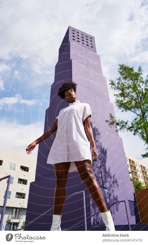 Stylish black woman posing on street against purple high rise building in downtown dress fashion trendy outfit female architecture style streetlamp urban