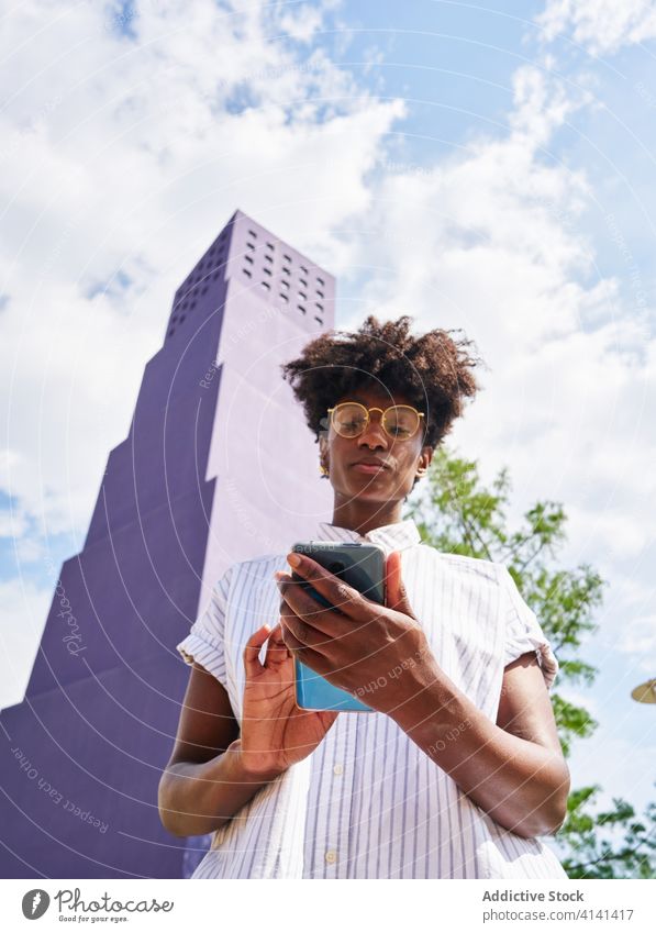Stylish black woman phoning on street against purple high rise building in downtown phone call talk dress smartphone fashion trendy outfit discuss conversation